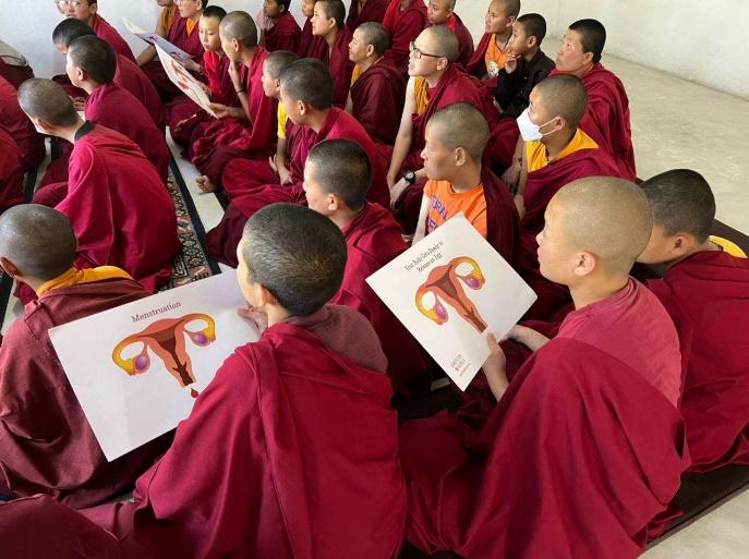 Nuns in Bhutan sit in red robes, heads shaved, attending a menstrual health workshop