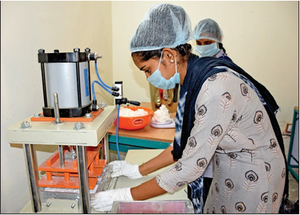 An Indian woman wearing basic PPE over her sari works with a small machine to help manufacture sanitary products